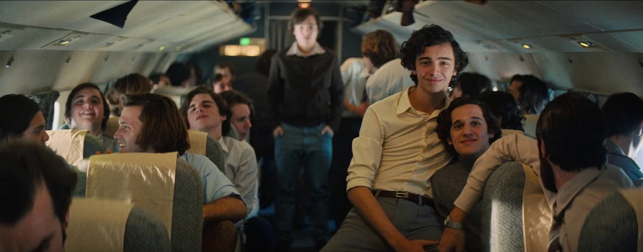 Society of the Snow (2023) movie still: medium — The interior of a crowded passenger airplane cabin features blue upholstered seats and narrow…
