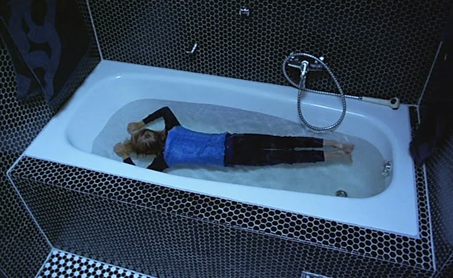 Possession (1981) movie still: wide — A bathroom features walls and floor covered in small hexagonal black and white tiles. A person lies submerged…