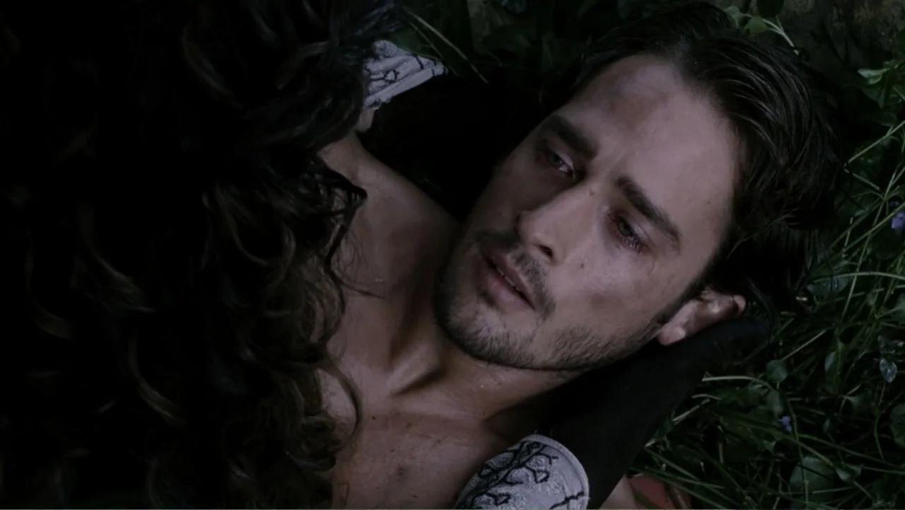 Van Helsing (2004) movie still: closeup — A man lies on damp grass at night surrounded by shadows and foliage. A woman cradles the man's head while…