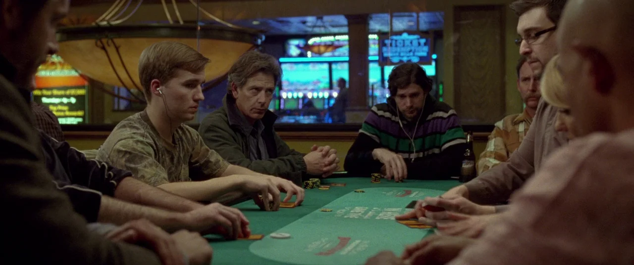 Mississippi Grind (2015) movie still: medium — A group of men sit around a green poker table in a dimly lit room. Neon signs for ticket redemption…