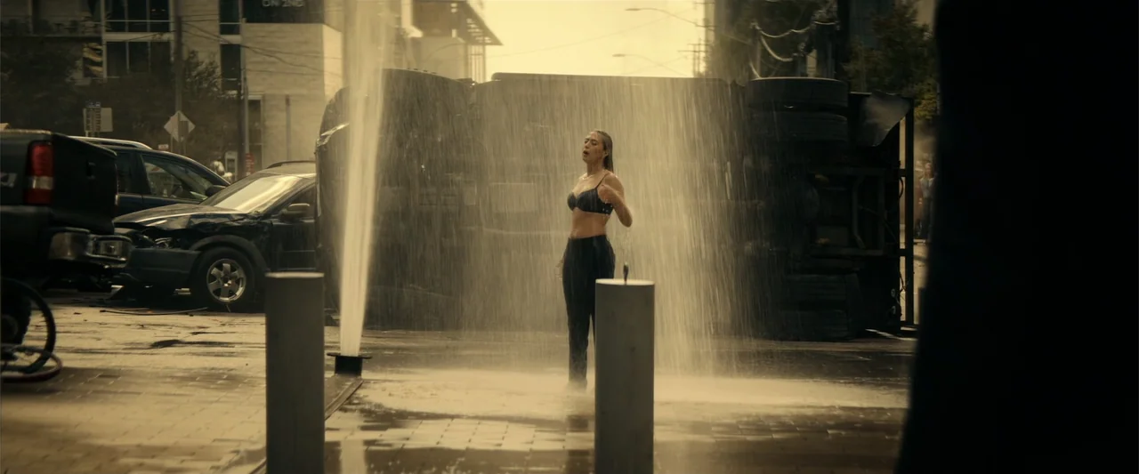 Hypnotic (2023) movie still: medium — A city street features a crashed truck on its side near a fountain spray. A woman stands in the middle of the…