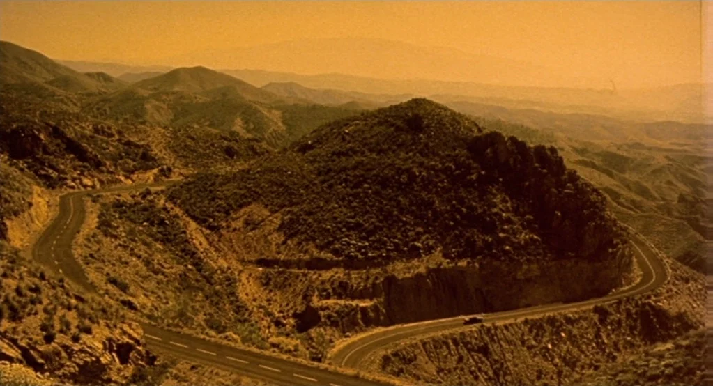 Morvern Callar (2002) movie still: establishing — A winding asphalt road cuts through a vast, dry landscape of arid, scrub-covered mountains. A…