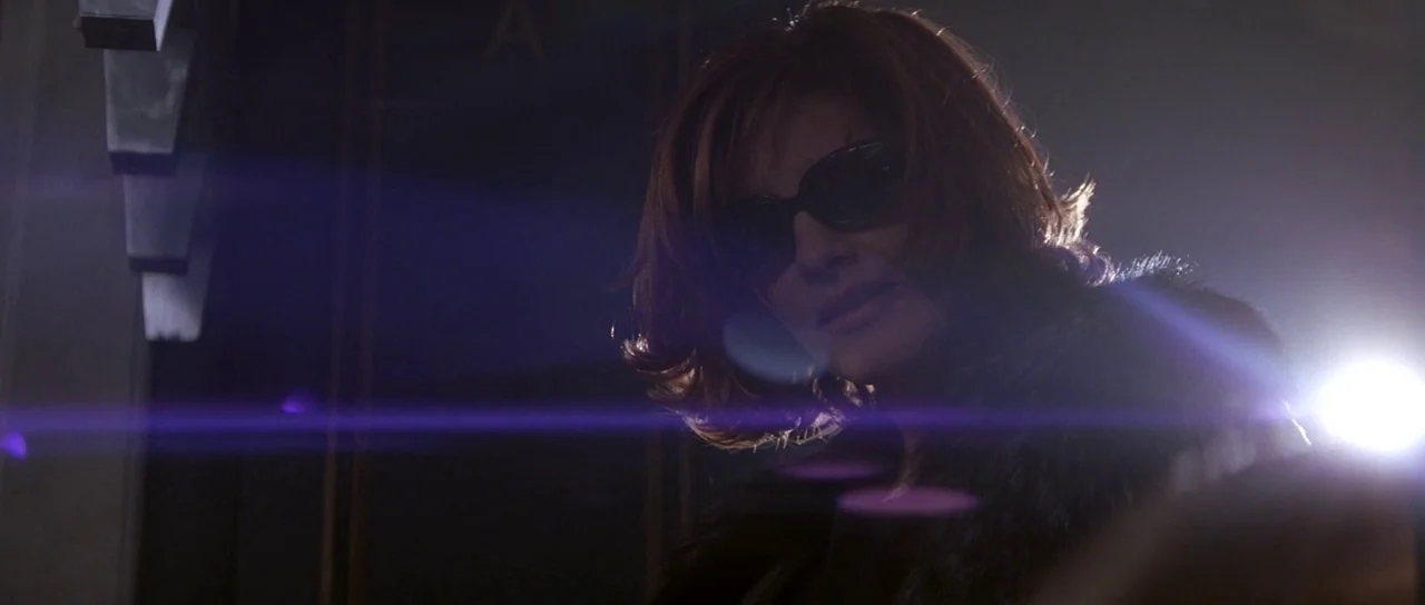 The Thomas Crown Affair (1999) movie still: closeup — A dark city street at night with an unidentified structure in the background. A woman wearing…