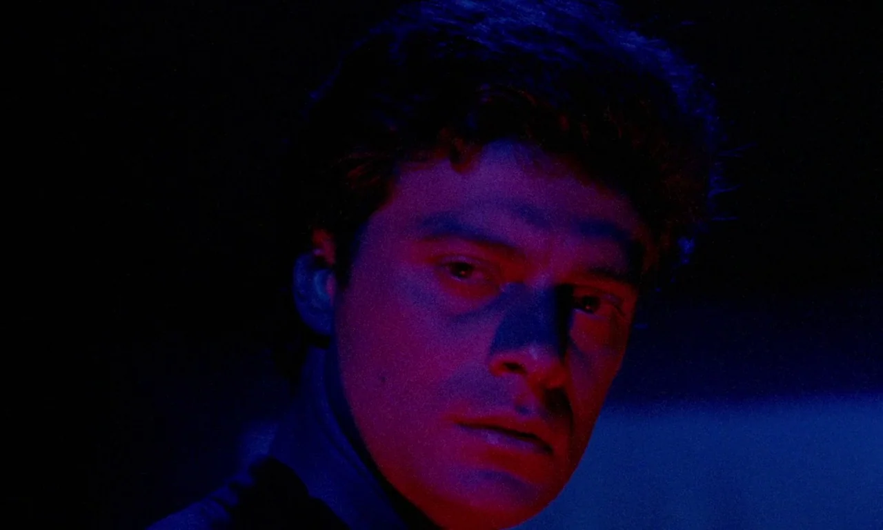 Paganini Horror (1989) movie still: closeup — A dark, unidentifiable interior space is illuminated only by narrow bands of colored light. A young…
