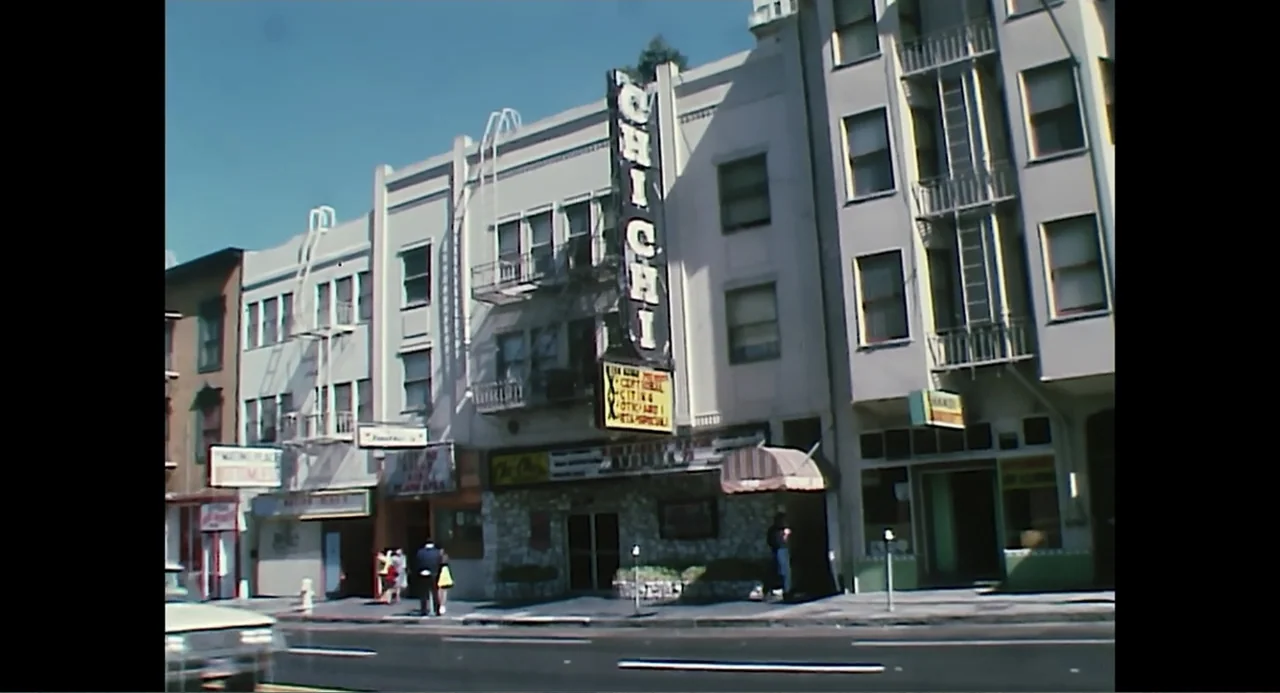 Free Chol Soo Lee (2022) movie still: wide — A multi-story building facade features a prominent neon sign for the Chi Chi club. Several storefronts…
