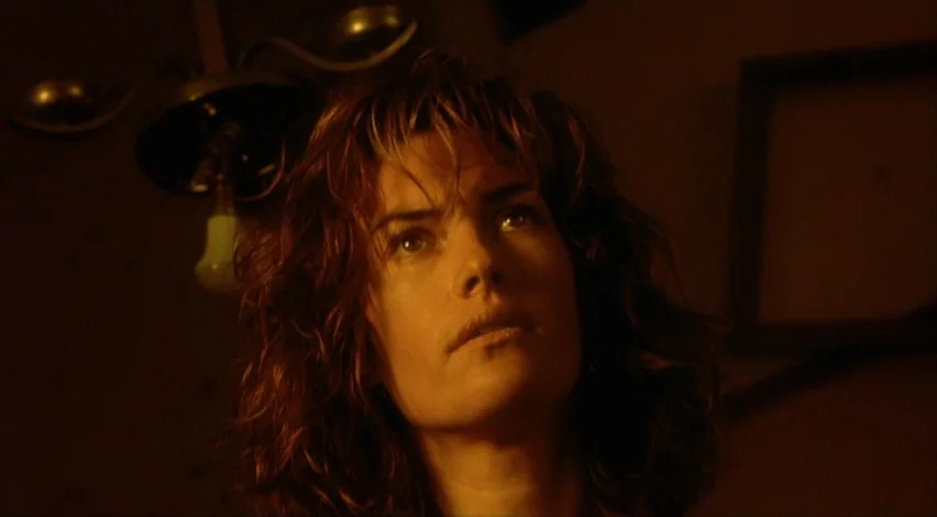 Dust Devil (1992) movie still: closeup — A dimly lit space features a low-hanging practical lamp above a person's head. The person gazes upward…