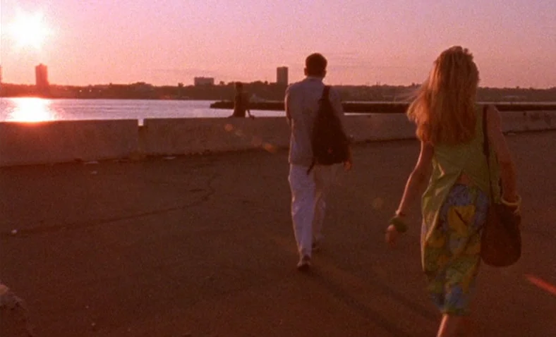 Paris Is Burning (1990) movie still: fullbody — A wide paved pier stretches along a body of water during the sunset. A man and a woman walk away…