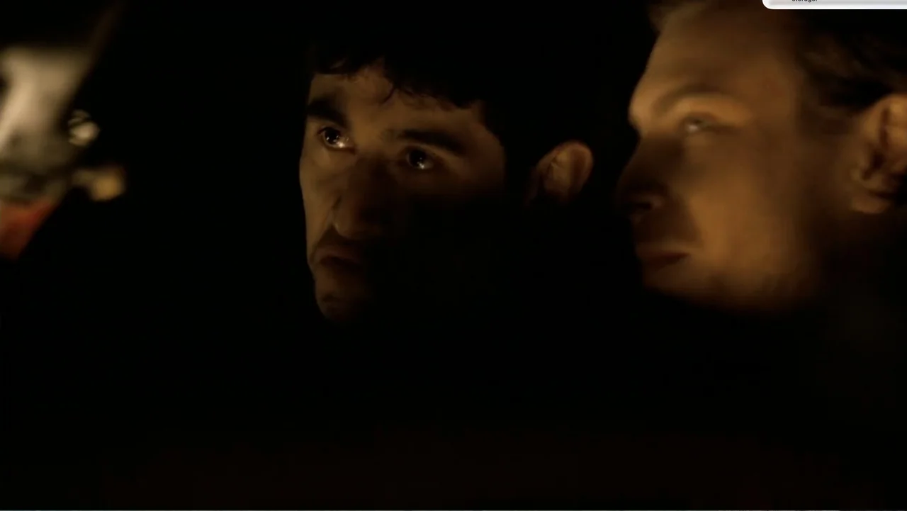 Chain Letter (2010) movie still: closeup — Two men sit together in a dark space, illuminated only by a harsh side light. They both direct their gaze…
