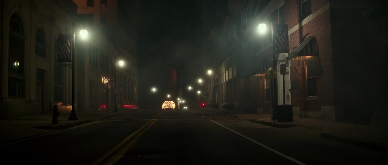 The Purge: Election Year (2016) movie still: establishing — A quiet urban street at night is lined with brick buildings and tall streetlamps. Thick…