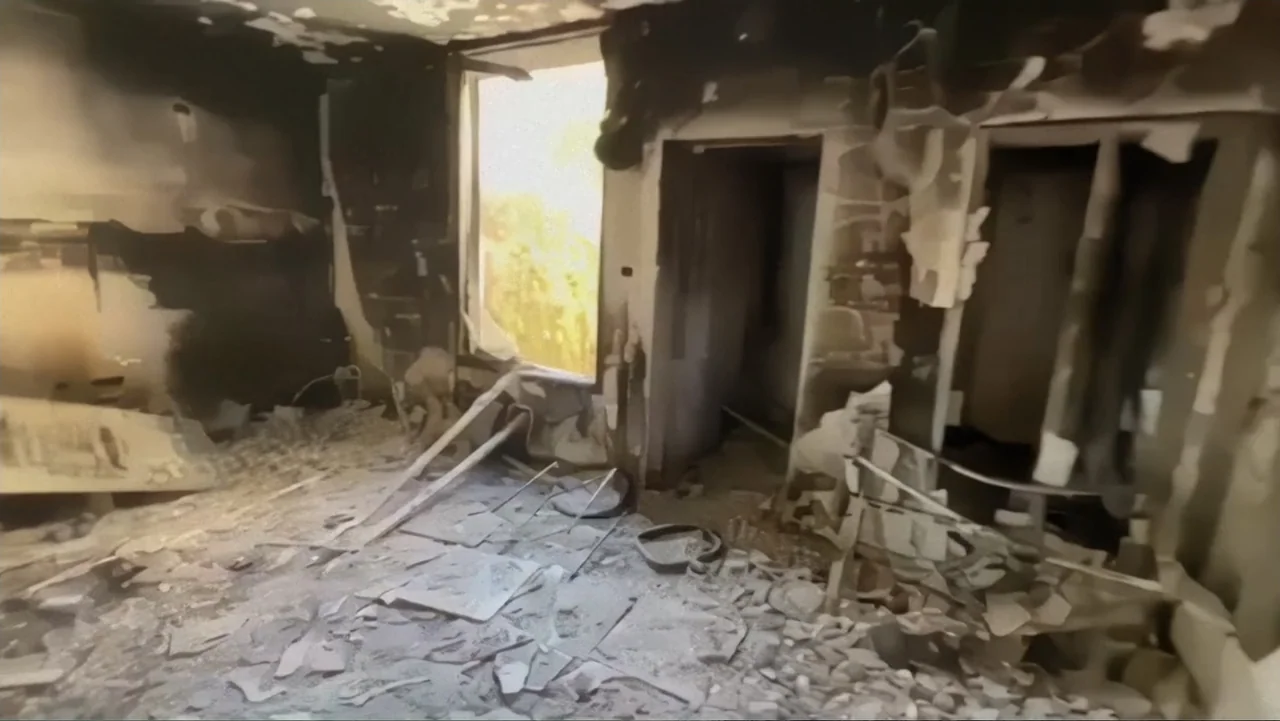 The Children of October 7 (2025) movie still: wide — A fire-damaged room features charred walls, piles of debris, and exposed structural remains. A…