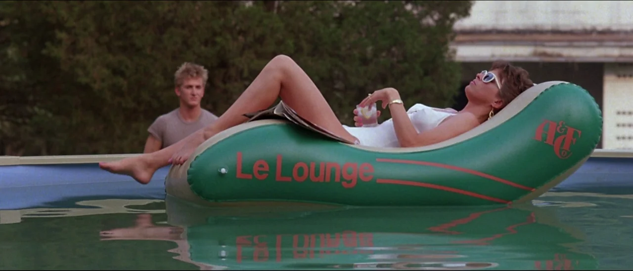 At Close Range (1986) movie still: fullbody — An above ground pool contains a woman on a green inflatable Le Lounge float. A young man stands in the…