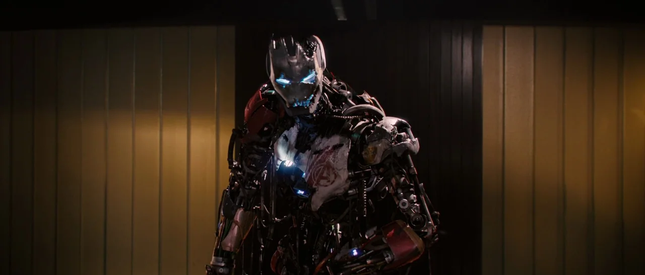 Avengers: Age of Ultron (2015) movie still: medium — A dark, industrial interior features walls lined with vertical panels of muted gold and black.…