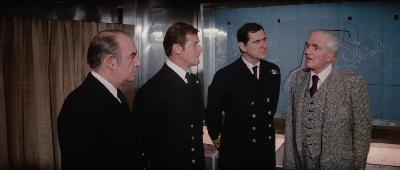The Spy Who Loved Me (1977) movie still: medium — Four men in professional attire stand inside a government or naval tactical command center. A…