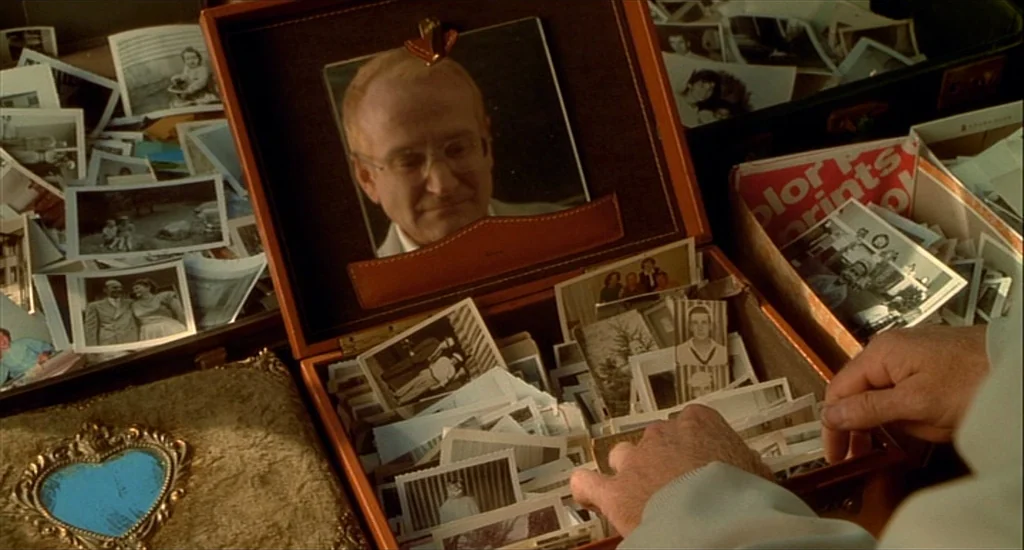 One Hour Photo (2002) movie still: closeup — A leather-bound case filled with numerous small vintage photographs sits on a flat surface. A man's…