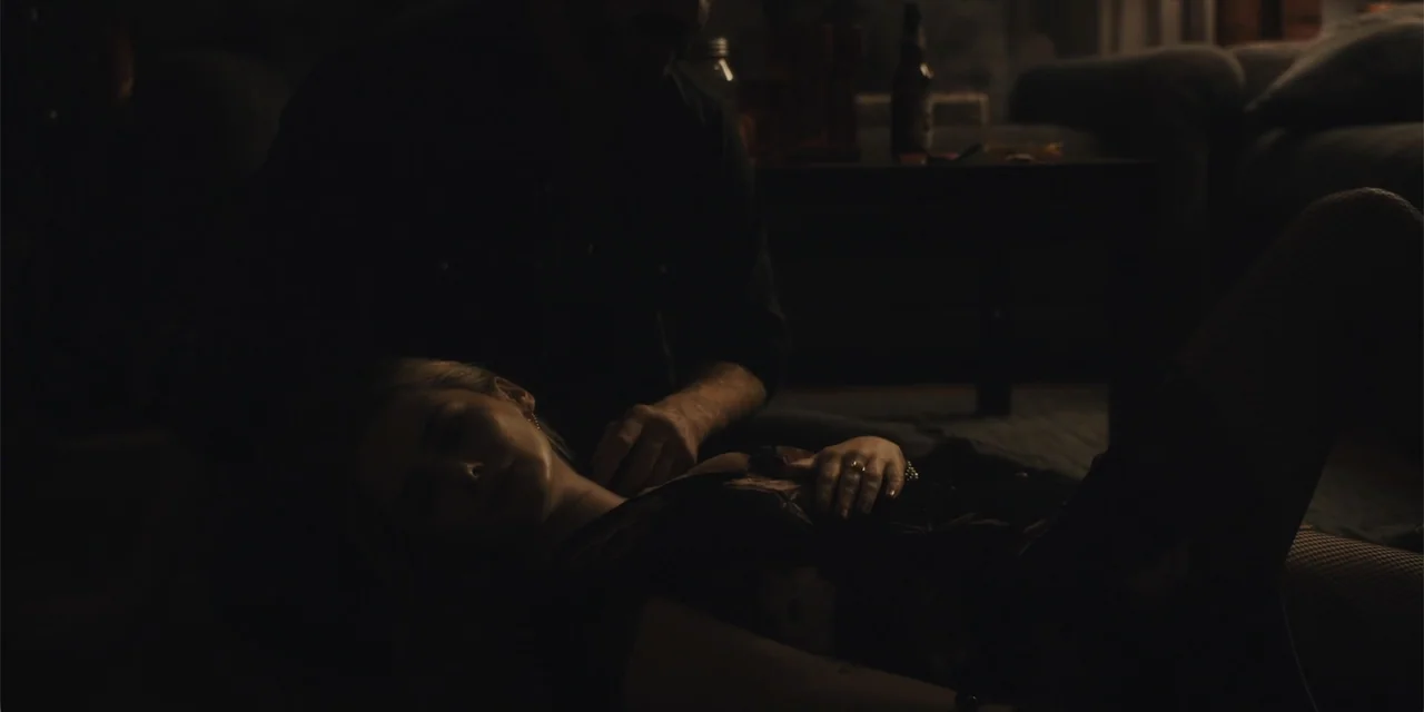 All Roads to Pearla (2019) movie still: medium — A dimly lit room contains a man and a woman resting on the floor. The woman reclines with her head…