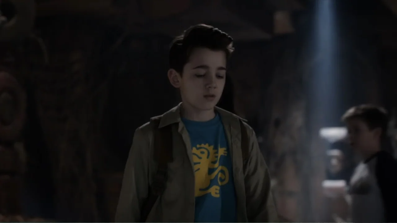 Legends of the Hidden Temple (2016) movie still: medium — A dimly lit indoor space with shadows obscuring the surroundings. A young boy stands with…