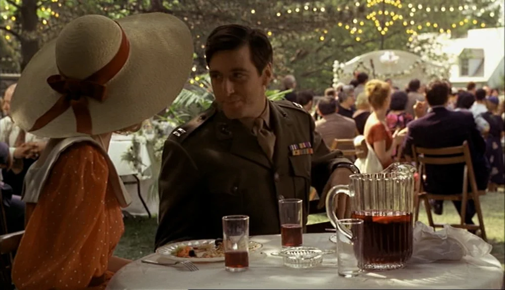 The Godfather (1972) movie still: medium — An outdoor wedding reception occurs under trees with fairy lights and numerous tables. A man in a…