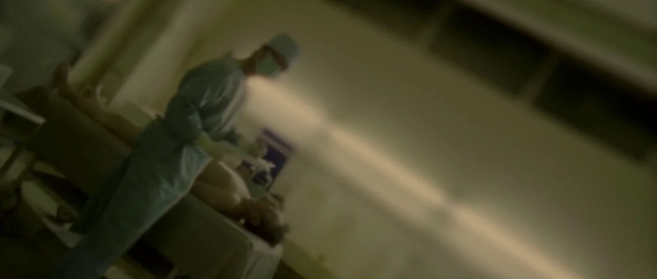 Enter The Void (2009) movie still: medium — A sterile medical room features a patient lying horizontally on a gurney. A medical professional in blue…