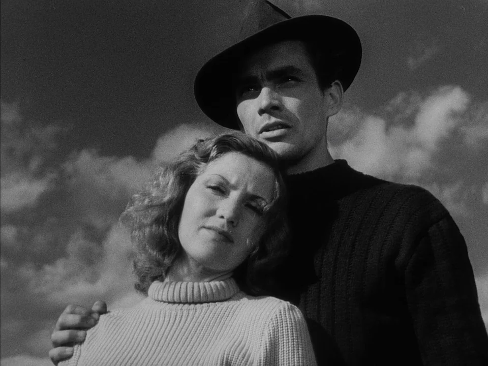 It Rains On Our Love (1946) movie still: medium — A man and a woman stand together against a backdrop of clouds in a field. The man has his arm…