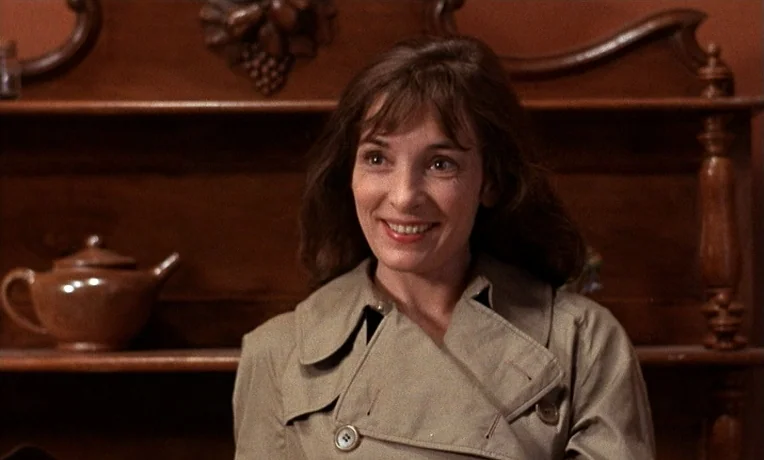 The Man Who Loved Women (1977) movie still: closeup — A woman stands before a dark wooden hutch in a room with painted walls. She looks ahead with a…