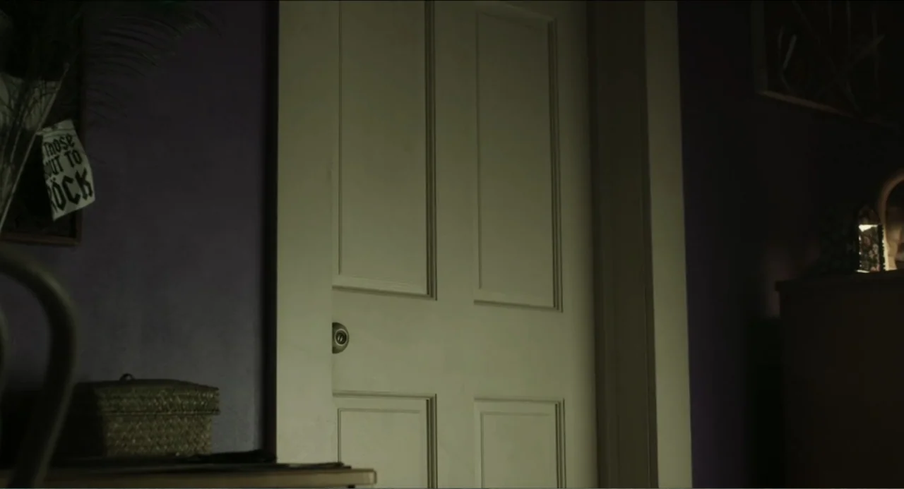 Haunter (2013) movie still: medium — A dark bedroom features a centrally located white door set against purple walls. The door remains closed while…