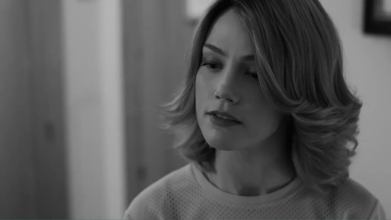 Creditors (2025) movie still: closeup — A well-lit indoor space features a woman in a textured top. The woman faces slightly away from the camera…