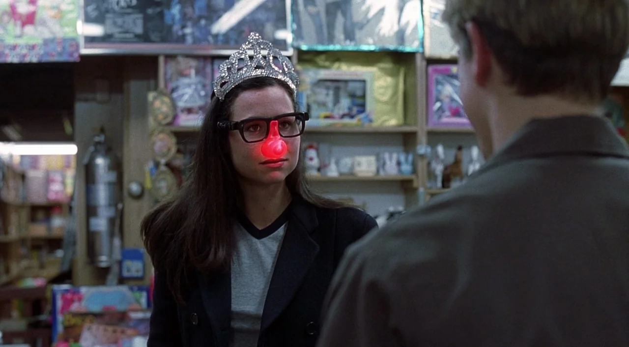 Good Will Hunting (1997) movie still: medium — A woman wearing a tiara and red clown nose stands in a cluttered retail aisle. She faces a man whose…