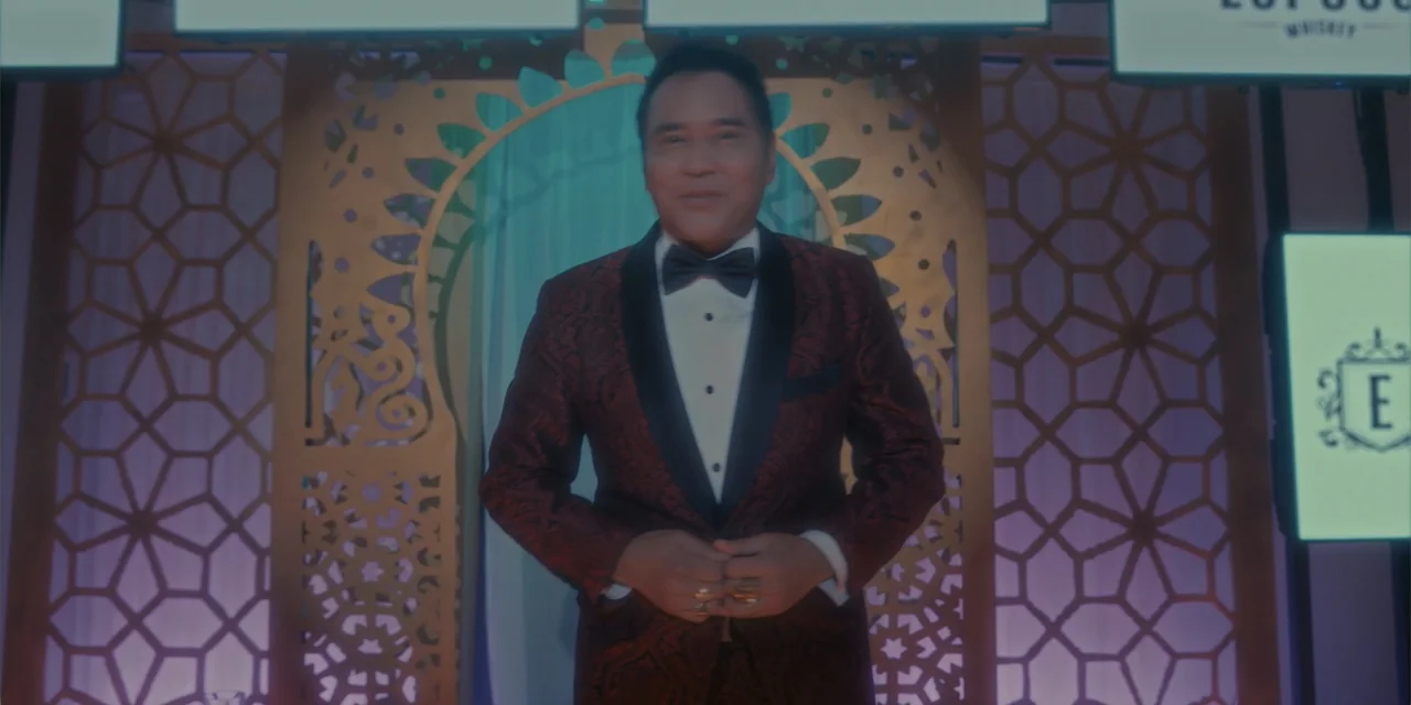Ten Little Mistresses (2023) movie still: medium — An indoor event stage features decorative gold lattice panels behind the central subject. A man…