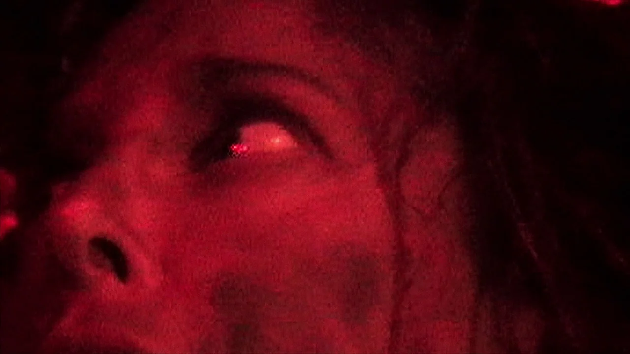 House of 1000 Corpses (2003) movie still: closeup — A close-up view of a person's face illuminated by intense red light. The individual looks upward…
