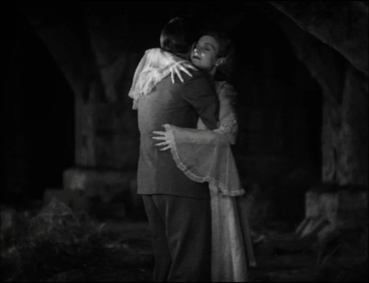 Dracula (1931) movie still: medium — A couple embraces among large, dark, crumbling stone architectural remains at night. The man faces away while…
