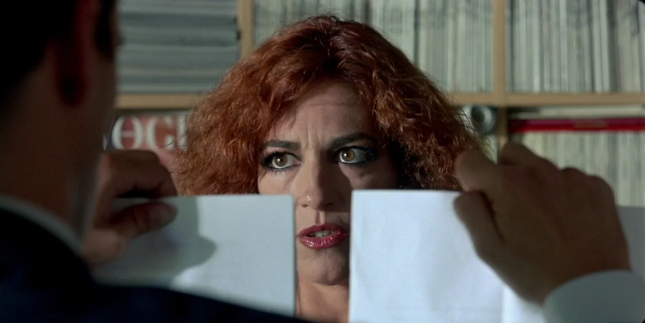 Law of Desire (1987) movie still: closeup — A workspace filled with files on shelves stands behind a woman and a man. The man holds a torn piece of…