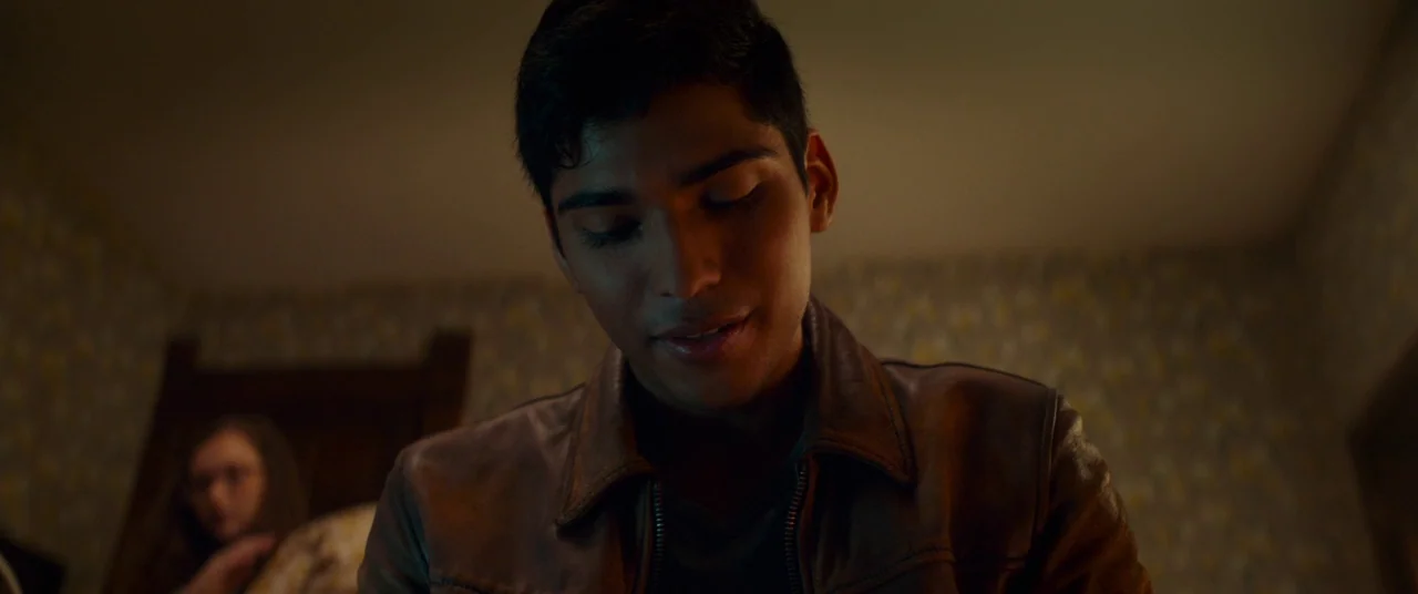 Scary Stories to Tell in the Dark (2019) movie still: closeup — A dimly lit room features patterned wallpaper and a dark wooden door frame. A young…