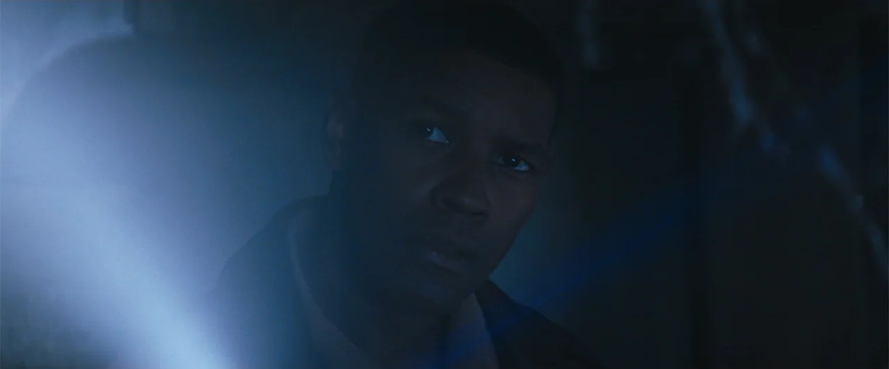 Fallen (2004) movie still: closeup — A dimly lit interior space filled with deep shadows and minimal environmental detail. A man stands in the dark,…