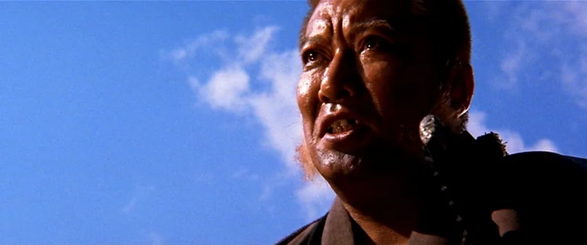 Lone Wolf and Cub: Sword of Vengeance (1972) movie still: closeup — A man stands against a bright blue sky with scattered clouds. The man looks…