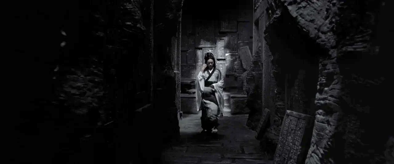 Shadow (2018) movie still: fullbody — A narrow corridor flanked by high, rough-hewn stone walls covered in carved ancient script. A woman in…