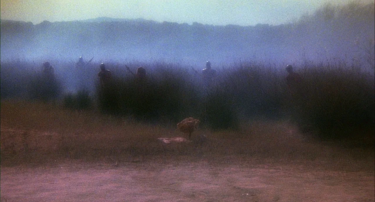 Conquest (1983) movie still: wide — A flat field is covered in a thick, low-hanging blue fog. Several armored figures stand partially hidden among…