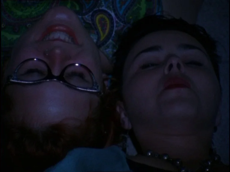 Totally F***ed Up (1993) movie still: closeup — Two women lie together on a surface in a dimly lit indoor space. They are seen from above while…
