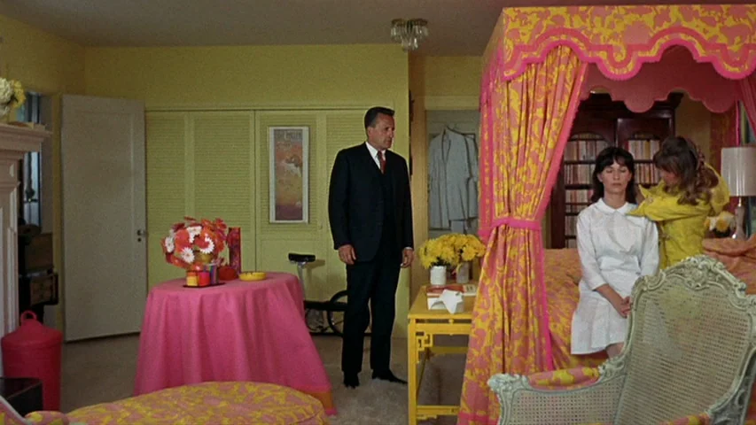 Petulia (1968) movie still: fullbody — A room with bright yellow walls and a canopy bed with pink patterned fabric. A man stands in the center while…