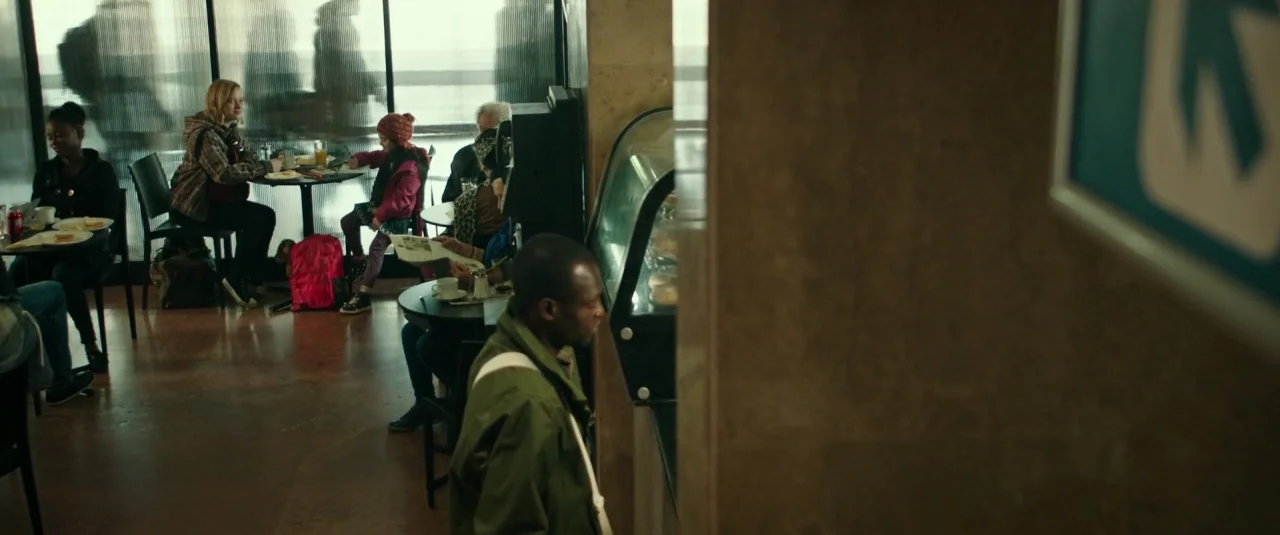 Don’t Breathe (2016) movie still: wide — A bustling public cafeteria with floor-to-ceiling windows showing blurred silhouettes of passing…
