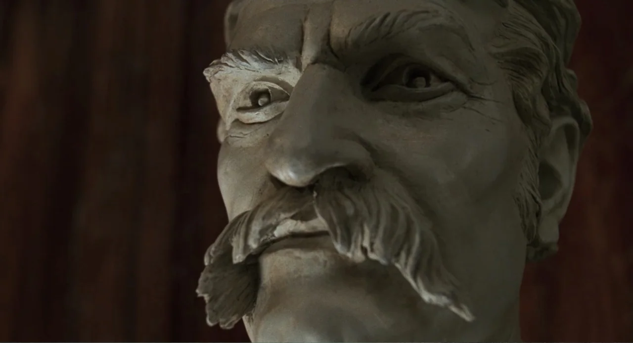 Jumanji (1995) movie still: closeup — A clay bust of a man with a prominent mustache sits in a studio. The sculpture features deep details in the…