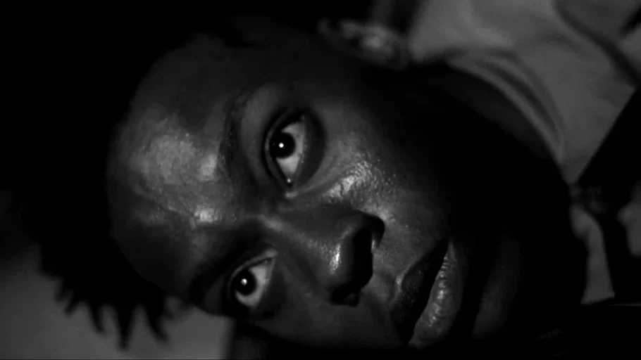 American History X movie still: closeup — A dimly lit, shadow-filled environment obscures most background details behind the subject. A person lies…