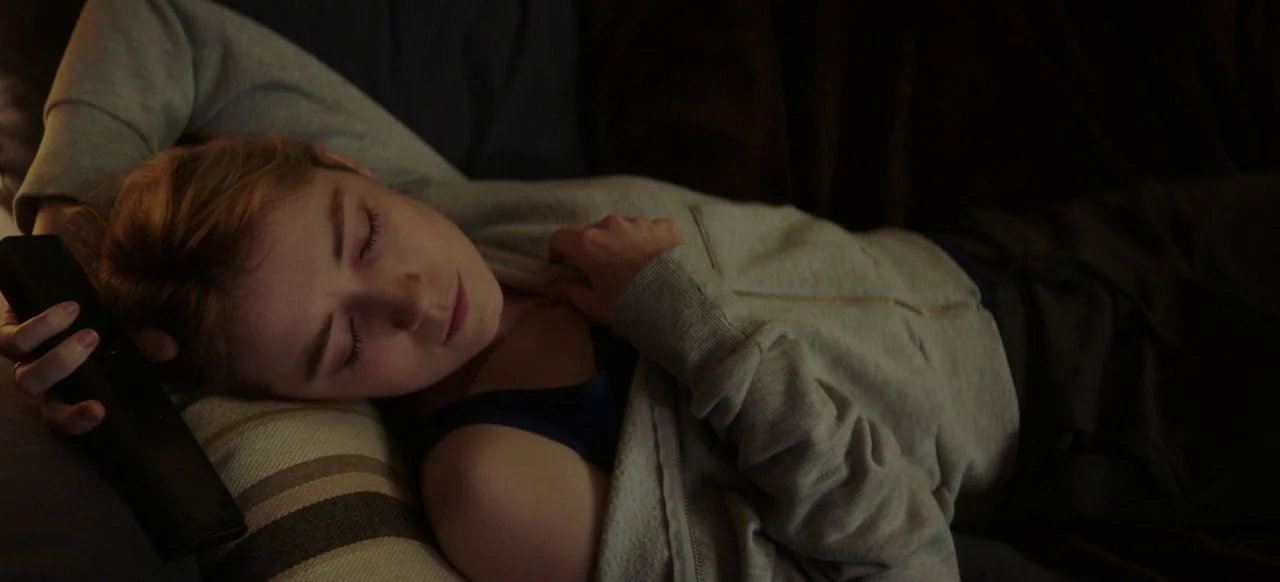 A Good Woman Is Hard To Find (2019) movie still: closeup — A person rests their head on a striped pillow in a darkened environment. They hold a…