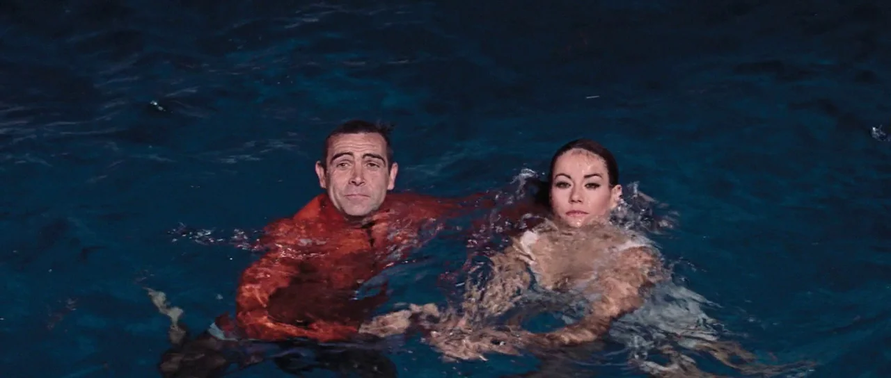 Thunderball (1965) movie still: medium — Two individuals are submerged to their chests in dark, rippling open water at night. They tread water…
