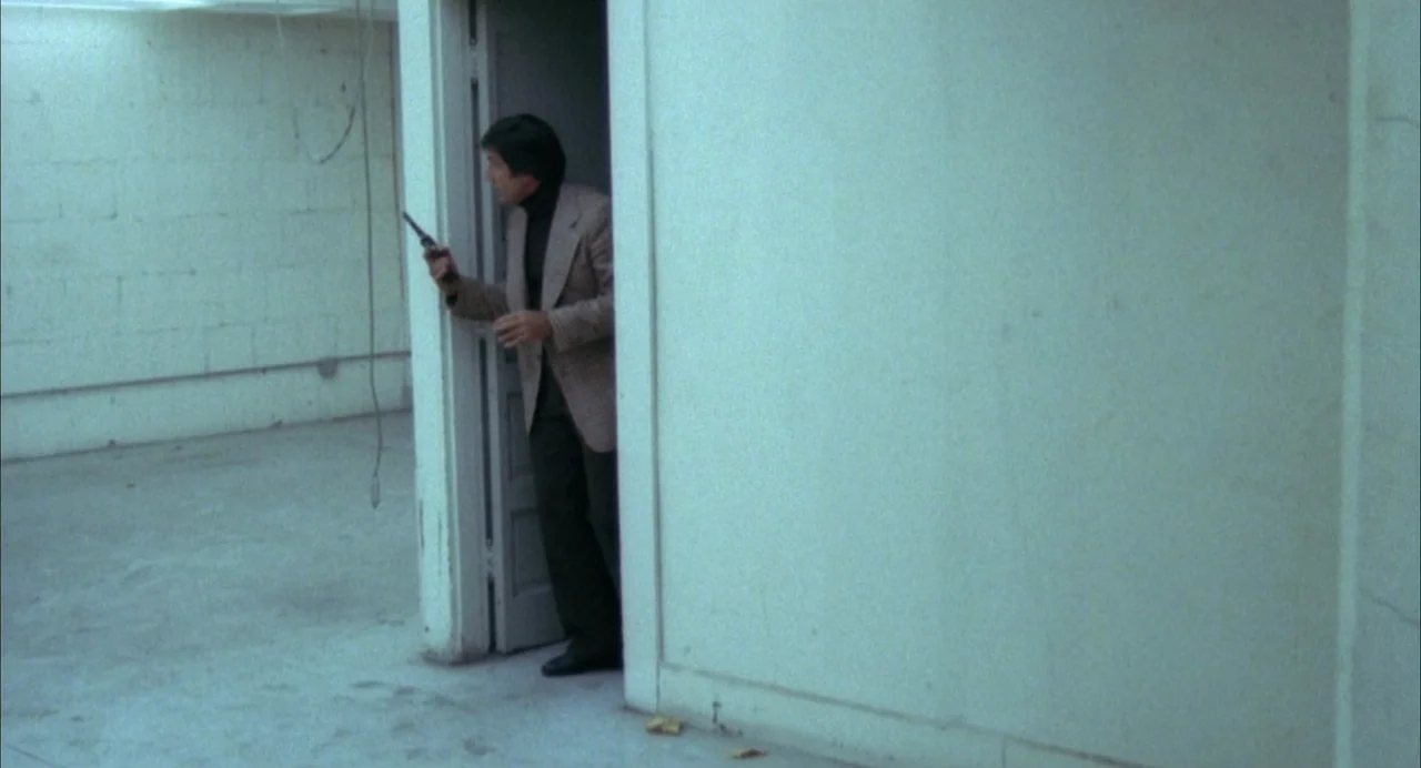 The Killing of a Chinese Bookie (1976) movie still: medium — A stark room with bare white masonry walls and a concrete floor. A man steps cautiously…