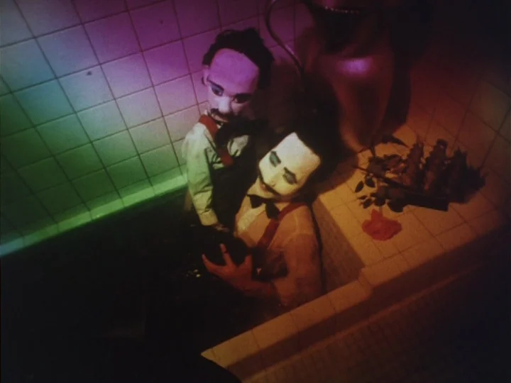 Butterfly (1974) movie still: medium — A dark, empty tiled bathtub contains a man and a hand-held puppet. The man wears stage makeup and sits in the…