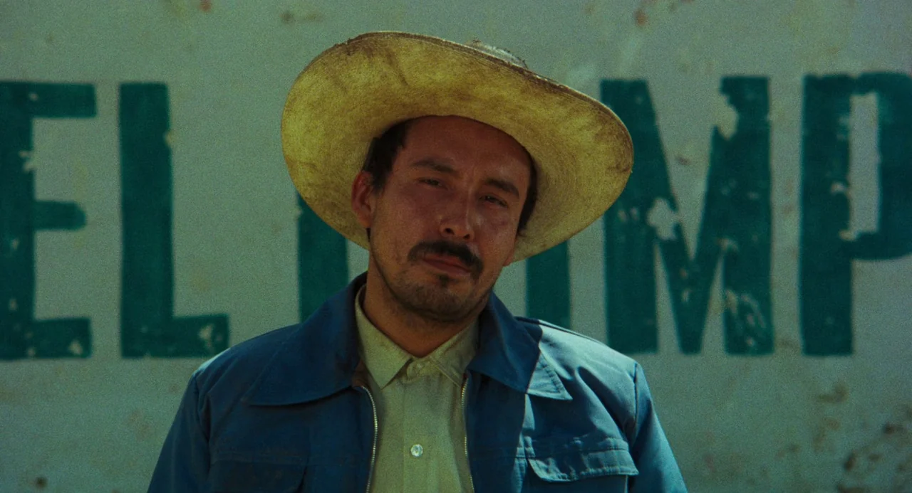 Canoa: A Shameful Memory (1976) movie still: closeup — A man stands in front of a weathered wall with faded green painted letters. The subject wears…