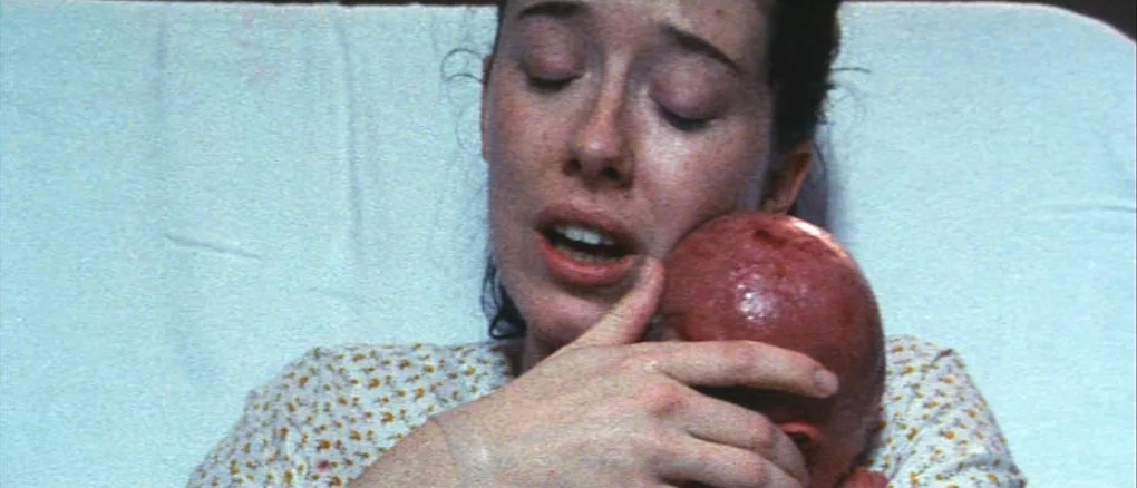 Wonderland (1999) movie still: closeup — A hospital bed with light-colored, crinkled sheets provides the background. A woman in a floral hospital…