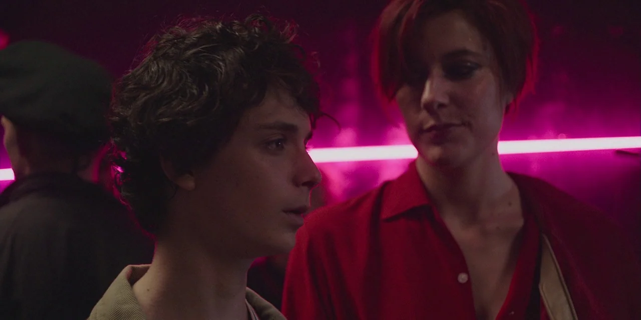 20th Century Women (2016) movie still: medium — A dimly lit interior space with a bright pink neon light in the background. A young man and a woman…