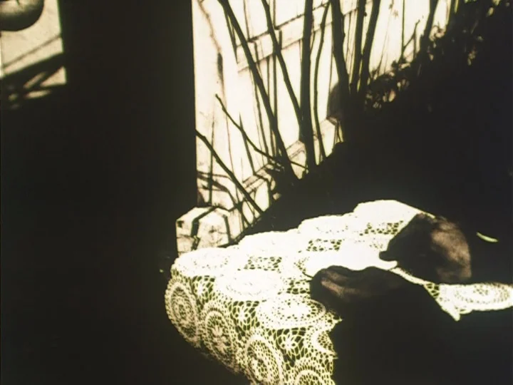 The Reading Machine (1977) movie still: closeup — A detailed white lace tablecloth is draped over a surface in an interior space. Strong sunlight…
