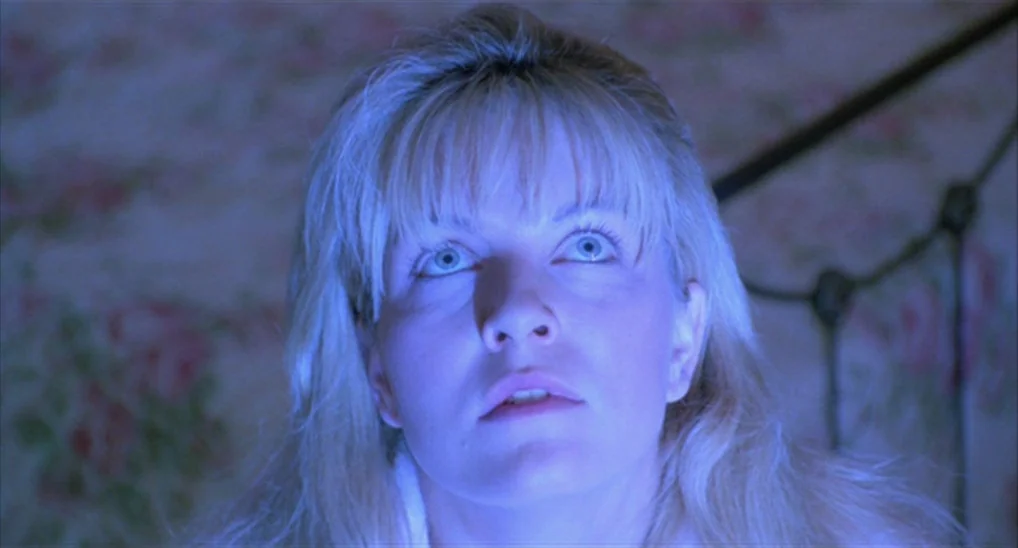 Twin Peaks: Fire Walk With Me (1992) movie still: closeup — A woman stares upwards while bathed in a blue light in a dimly lit room. Floral…